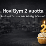 HoviGym 2 vuotta – tumma ja blurattu kuntosali tausta sekä kynttilällä varustettu kakkonen cupcake päällä
